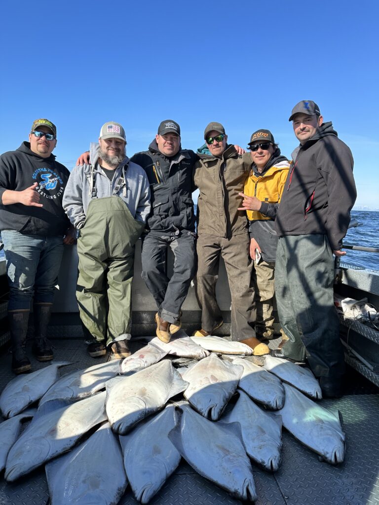 Group of anglers posing with a large catch of halibut on a fishing boat.